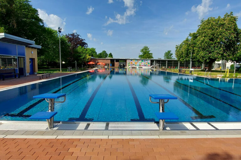 Freibad mit Startblöcken,blauem Wasser und buntem Wandbild im Hintergrund