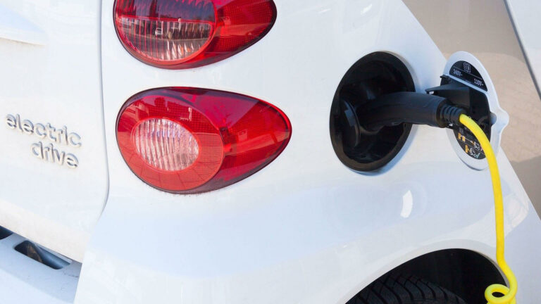 Weißes Elektroauto wird an der Ladestation mit gelbem Kabel aufgeladen