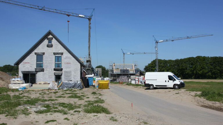 Zwei im Bau befindliche Häuser mit Baukränen und einem weißen Transporter auf einer Baustelle