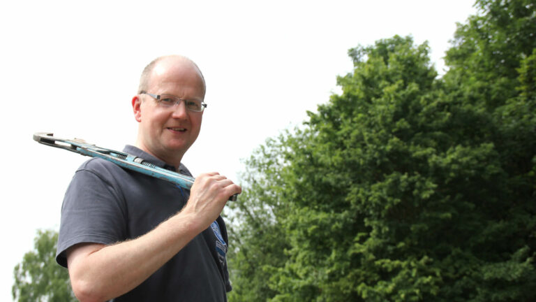 Installateur mit Brille und grauem T-Shirt trägt Rohrzange auf Schulter