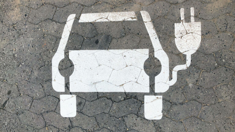Weißes Symbol eines Elektroautos mit Ladestecker auf grauem, rissigem Asphalt