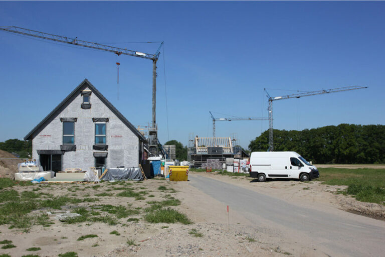 Baustelle mit Gebäuden im Rohbau, zwei großen Baukränen und einem weißen Transporter auf einem Weg