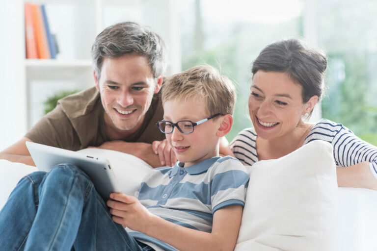 Lächelnde Familie mit Vater, Mutter und Sohn, der eine Brille trägt, schaut gemeinsam auf ein Tablet