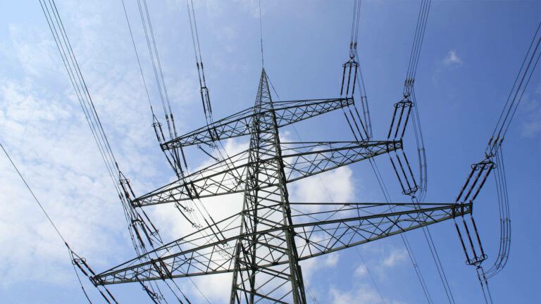 Stahlgittermast eines Hochspannungsmastes vor blauem Himmel mit Wolken