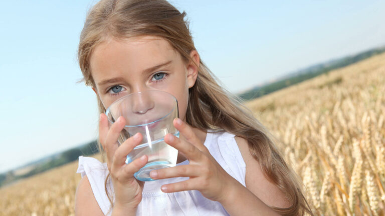 Mädchen auf einem Feld das ein Glas Wasser trinkt