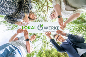 Vier Personen halten ein Banner mit der Aufschrift "LokalWerke" unter einem Baum