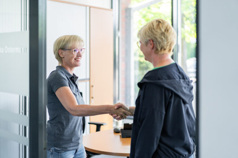Zwei Frauen mit kurzen blonden Haaren schütteln sich in einem hellen Büro die Hand