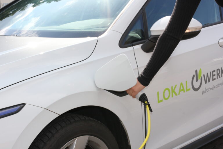 Hand steckt Ladekabel in weißen Elektroauto mit Aufschrift 
