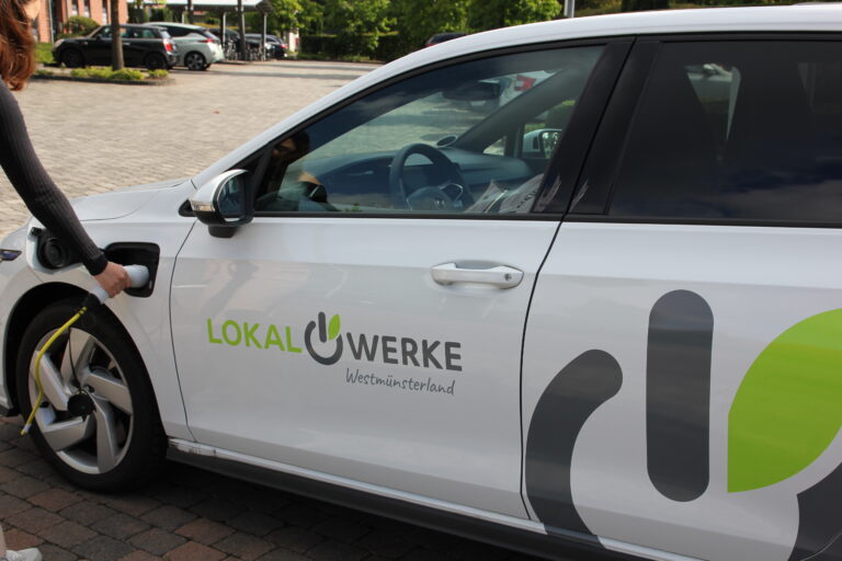 Weißes Elektroauto mit Aufschrift 'Lokalwerke Westmünsterland' wird an Ladestation aufgeladen
