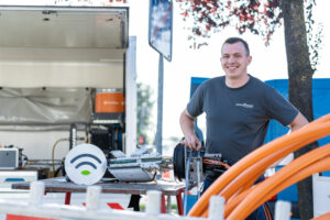 LokalWerke Techniker steht lächelnd neben Glasfaserkabeln vor einem offenen Transporter