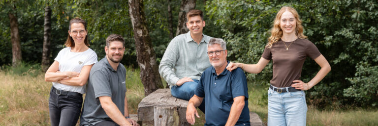 Drei Männer und zwei Frauen sitzen und stehen um einen Picknicktisch herum im Wald.
